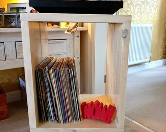May include: A white wooden record player stand with hairpin legs. The stand has a shelf for records and a top shelf for a record player. The stand is decorated with a red "WOW!" sign.