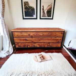 May include: A rustic wooden chest with three drawers and a black metal frame. The chest is sitting on a white fluffy rug.