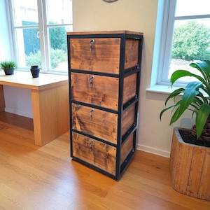 Könnte beinhalten: Ein Holzschrank mit vier Schubladen, jede mit Schlüsselloch und dunklem Metallrahmen. Das Holz hat eine warme, natürliche Oberfläche. Der Schrank steht in einem Raum mit Schreibtisch, Stuhl und Topfpflanze.
