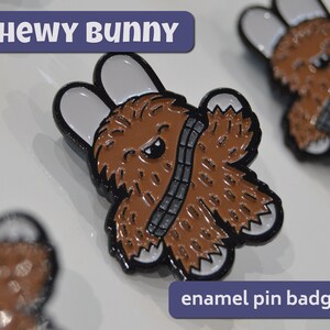 May include: Chewy Bunny enamel pin badge featuring a brown furry bunny with a black bandolier and white ears. The text "Chewy Bunny" is in a blue banner above the pin and "enamel pin badge" is in a blue banner below the pin.