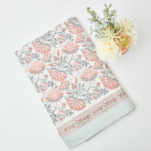 May include: A white tablecloth with a floral pattern in shades of pink and green. The tablecloth has a border with a striped pattern in white and green.