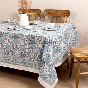 May include: A rectangular tablecloth with a blue floral pattern, set on a wooden table. The tablecloth has a white border and is paired with matching napkins and placemats. The table is set with plates, bowls, and wine glasses.