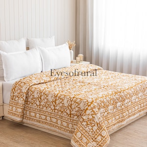 Peut inclure: Une courtepointe à motifs floraux jaune moutarde et blancs sur un lit avec des oreillers blancs. La courtepointe présente un motif floral répétitif et une bordure décorative. Le texte "Eyesofrural" est visible.