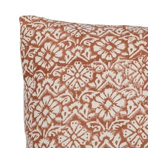 May include: A close-up of a throw pillow with a white and orange floral pattern. The pillow is made of a soft, textured fabric.