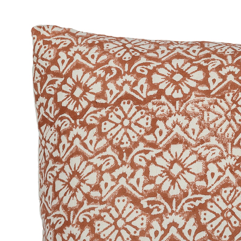 May include: A close-up of a throw pillow with a white and orange floral pattern. The pillow is made of a soft, textured fabric.