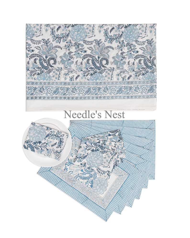 May include: A collection of blue and white floral patterned table linens. The set includes a tablecloth, napkins, and placemats. The tablecloth features a large floral design, while the napkins and placemats have a smaller floral pattern and striped borders. The brand name "Needle's Nest" is visible.