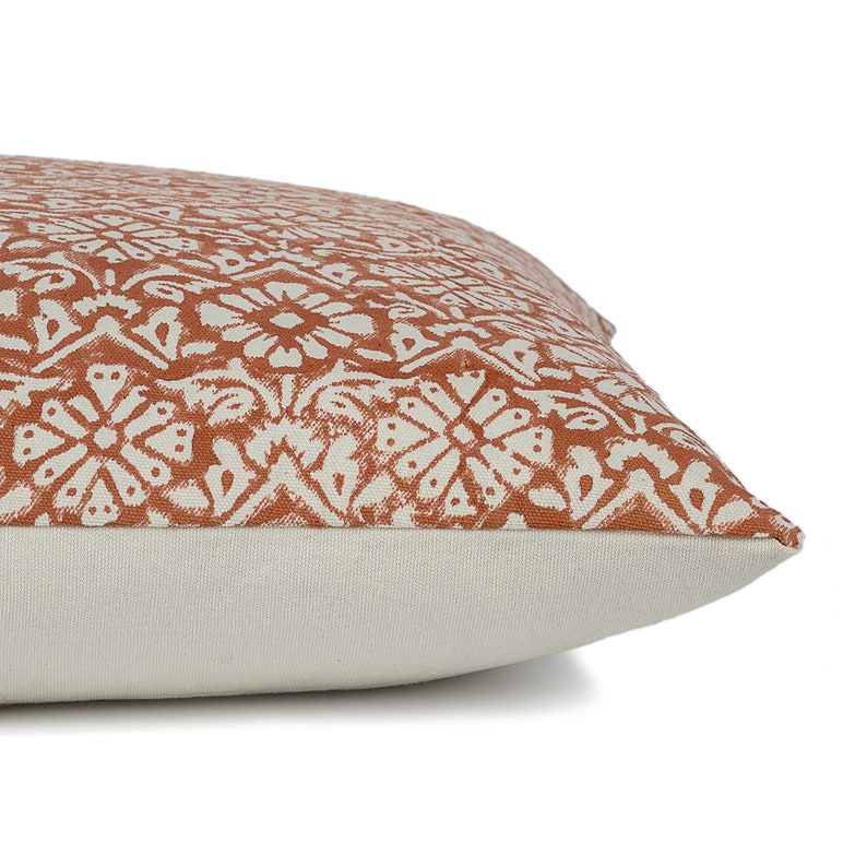 May include: A rust-colored throw pillow with a white geometric pattern. The pillow has a white border and a white back.