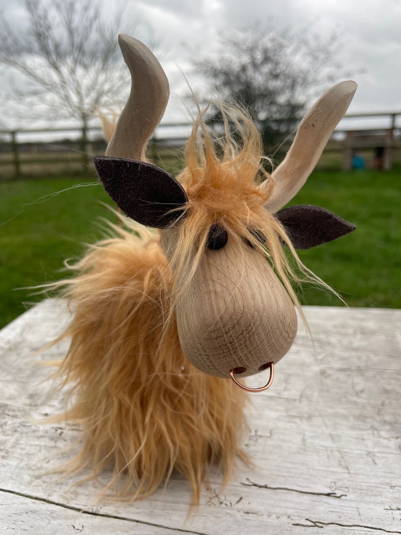 Peut inclure: Une vache &eacute;cossaise en bois jouet avec une fourrure brune et un anneau de nez en cuivre. La vache a une longue crini&egrave;re hirsute et une expression amicale.