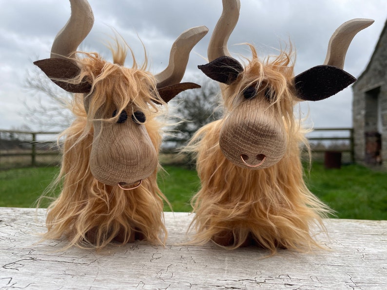 Peut inclure: Deux figurines de vache Highland en bois avec une fourrure brune, des yeux noirs et un nez brun. Chaque vache a un anneau m&eacute;tallique autour du nez.