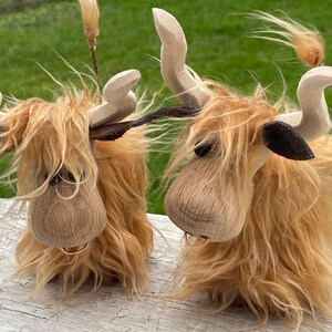Peut inclure: Deux figurines de vache Highland en bois avec une fourrure brune et des oreilles noires. Les vaches ont un anneau autour du cou et sont debout sur une surface en bois.