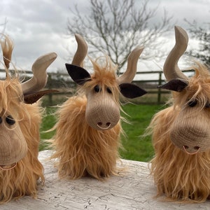 Peut inclure: Trois figurines de vache &eacute;cossaise en bois avec une fourrure brune, des yeux noirs et des cornes en bois. Les vaches sont debout sur une surface en bois.
