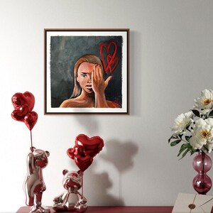 May include: A framed artwork depicts a woman covering one eye with her hand, with red heart shapes drawn on the background. Two shiny, red heart-shaped balloons are attached to a silver bear figurine. A second bear figurine is also visible.