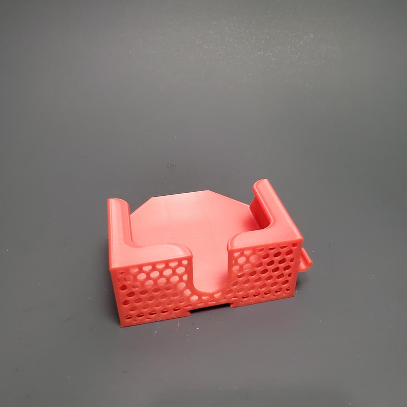 K&ouml;nnte beinhalten: Ein korallenfarbener, 3D-gedruckter Kartenhalter. Der Halter hat eine rechteckige Basis mit zwei aufrechten Seiten mit einem Wabenmuster. Das Design umfasst einen zentralen Bereich zum Halten von Karten und zwei abgewinkelte St&uuml;tzen.