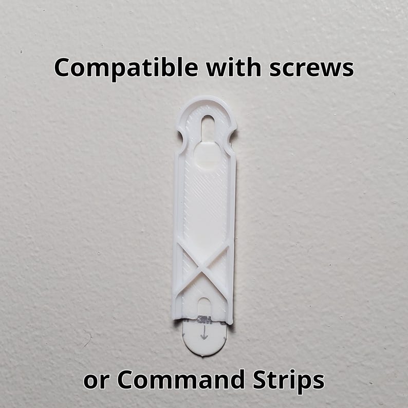 K&ouml;nnte beinhalten: Ein wei&szlig;er Wandhaken aus Kunststoff mit dem Text "Compatible with screws oder Command Strips." Der Haken hat eine rechteckige Form mit einem zentralen Schlitz und einem gew&ouml;lbten Oberteil. Er hat ein X-f&ouml;rmiges Design in der N&auml;he des Bodens.