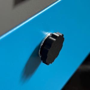 May include: Close-up of a black knob with a silver ring on a blue surface.