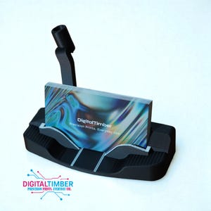 May include: A black business card holder with a stack of cards. The cards have a colorful, abstract design and the text "DigitalTimber Precision Prints. Everyday Use." The holder has a curved design and a black arm.