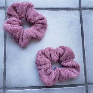 Może przedstawiać: Dwa różowe scrunchies z frotte. Scrunchies są wykonane z miękkiego, chłonnego materiału i idealnie nadają się do utrzymania włosów na miejscu.