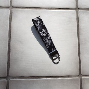 Correa de cordón de muñeca con llavero floral en blanco y negro