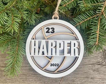 Puede incluir: Adorno de madera blanco con forma de balón de voleibol con el número 23 y el nombre "HARPER" en letras negras. El año 2022 también está incluido en el adorno.