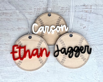 May include: Three wooden baseball-themed luggage tags with the names "Carson", "Ethan", and "Jagger" written in white, red, and black lettering, respectively.