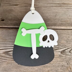 May include: A green, black, and white candy corn ornament with a white letter "T" and a white skull with black eye sockets.