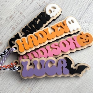 May include: Four wooden Halloween name tags with different colored backgrounds and Halloween-themed cutouts. The names are "Oliver", "Hadley", "Addison", and "Lucas".