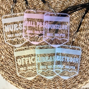 May include: Six clear acrylic badge holders shaped like pencils, each featuring a black lanyard. The badges are printed with white text including NURSE, HALL PASS, COUNSELOR, OFFICE, LIBRARY, RESTROOM, and the name MRS. HOLPER on each individual piece.