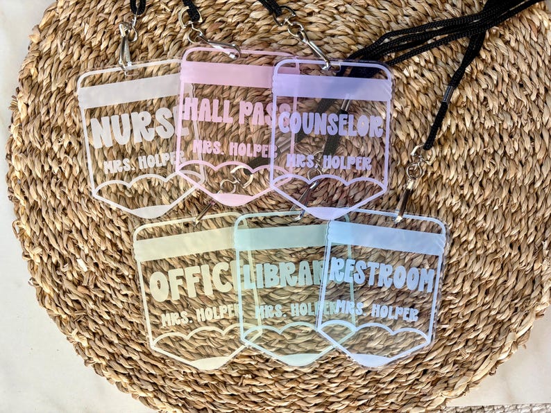May include: Six clear acrylic badge holders shaped like pencils, each featuring a black lanyard. The badges are printed with white text including NURSE, HALL PASS, COUNSELOR, OFFICE, LIBRARY, RESTROOM, and the name MRS. HOLPER on each individual piece.
