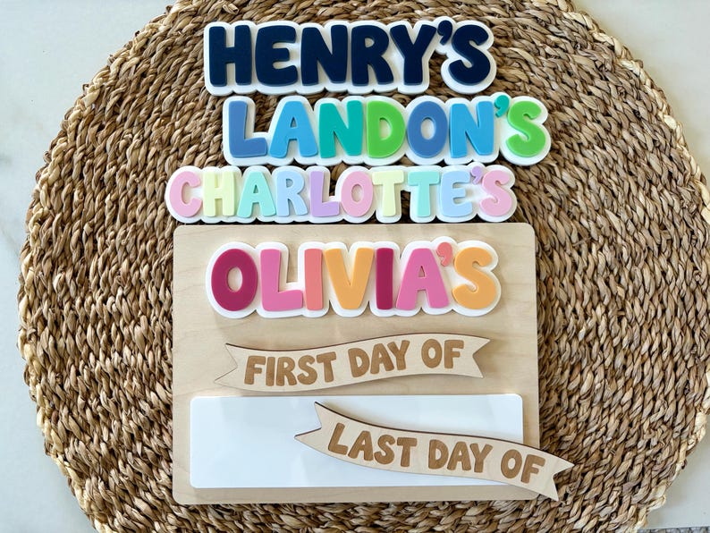 K&ouml;nnte beinhalten: Ein Holzschild mit gestapelten, bunten 3D-Buchstaben, die Henry's, Landon's, Charlotte's und Olivia's bilden. Darunter befinden sich zwei Holzbanner mit der Gravur First Day Of und Last Day Of &uuml;ber einer leeren, wei&szlig;en rechteckigen Fl&auml;che.