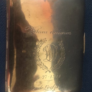 Op de afbeelding: Een gouden metalen sigarettenkoker met een gegraveerde inscriptie die "W dniu imienin" en "6-27-1920" en "od Lodzi" luidt.