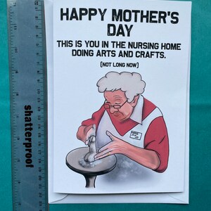 May include: A humorous greeting card with a cartoon illustration of an older person making pottery. The card reads "Happy Mother's Day. This is you in the nursing home doing arts and crafts. (Not long now)"
