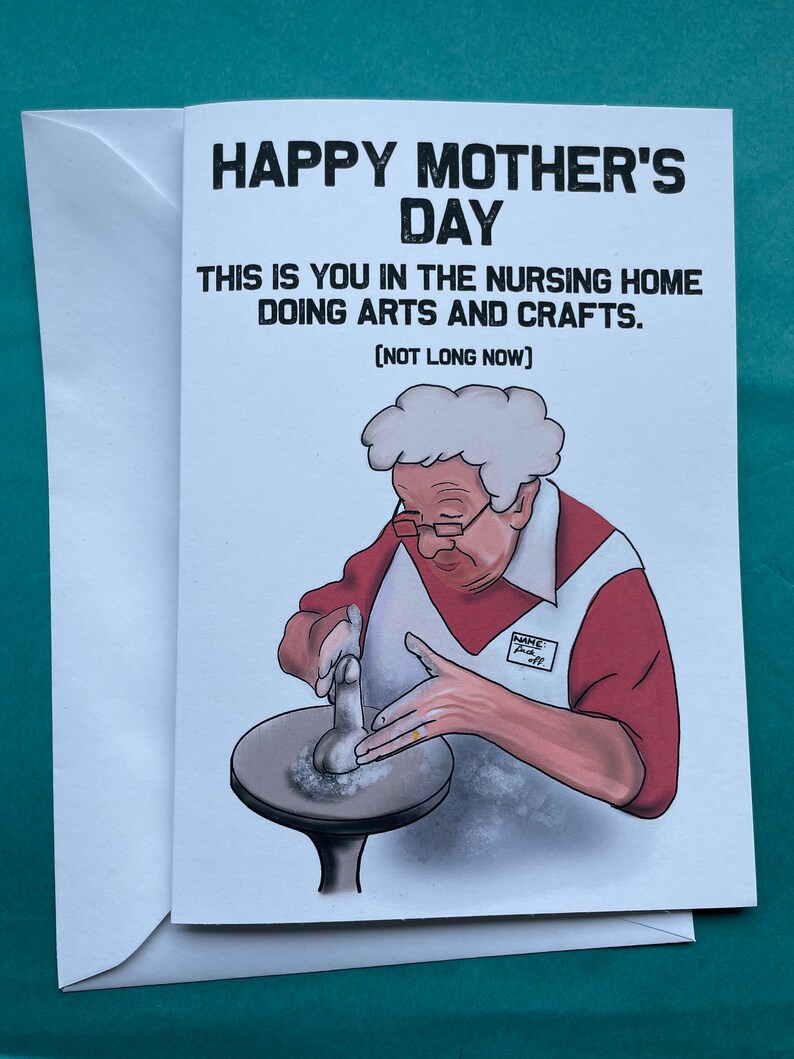 May include: A humorous Mother's Day card featuring a cartoon illustration of an older woman in a nursing home, wearing a red shirt and a white apron, working on a pottery wheel. The text reads "Happy Mother's Day. This is you in the nursing home doing arts and crafts. [Not long now]"