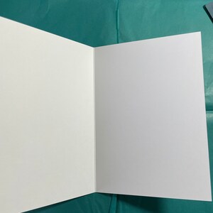 May include: A blank white card with a fold in the middle. The card is sitting on a teal blue surface.