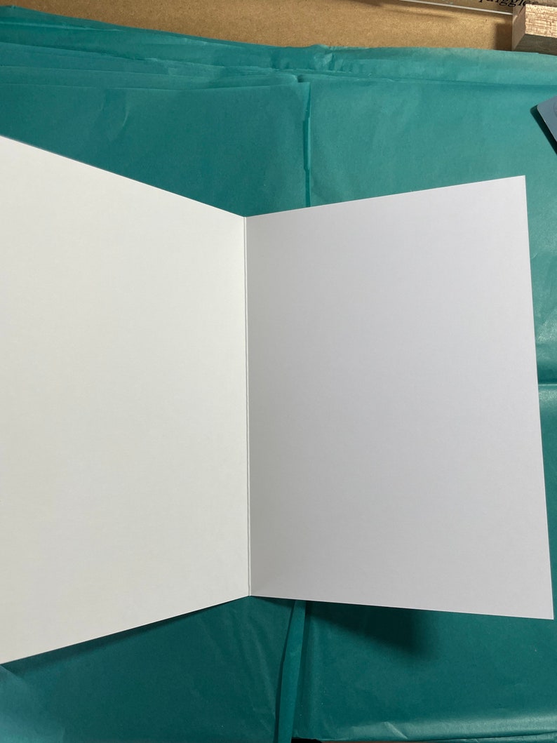 May include: A blank white card with a fold in the middle. The card is sitting on a teal blue surface.