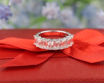 May include: A silver band ring with a row of emerald-cut diamonds set in a channel setting. The ring is on a red velvet box.