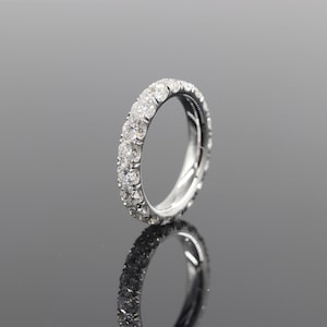 Op de afbeelding: Een zilveren eternity ring met een doorlopende rij rond geslepen diamanten. De ring is hoogglans gepolijst, reflecteert licht en creëert een schitterende glans. De diamanten zijn dicht op elkaar gezet en bedekken de hele band. De ring wordt gepresenteerd op een reflecterend oppervlak.