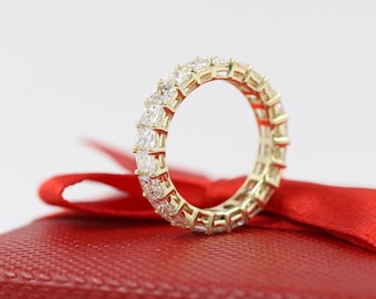 May include: A gold band ring with a row of square-shaped diamonds set in a continuous line around the band.