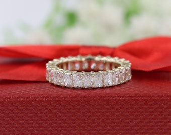 May include: A diamond eternity band with a row of rectangular-shaped diamonds set in a gold band. The ring is on a red velvet box.