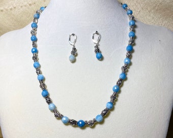 Könnte beinhalten: Ein blaues und silbernes Halsketten- und Ohrring-Set. Die Halskette besteht aus blauen Edelsteinperlen mit silbernen Akzenten. Die Ohrringe sind silberfarben mit blauen Edelsteintropfen.