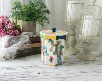 May include: A white octagonal wooden box with a blue knob lid. The box is decorated with colorful illustrations of clowns and confetti. The box is sitting on a whitewashed wooden surface.