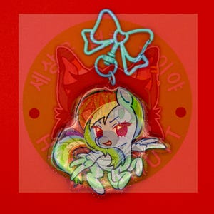 May include: A glittery acrylic keychain featuring a cartoon pony with a rainbow-colored mane and tail, red eyes, and light green skin. The pony is attached to a light blue bow-shaped metal clasp. The design includes a subtle sparkle finish.