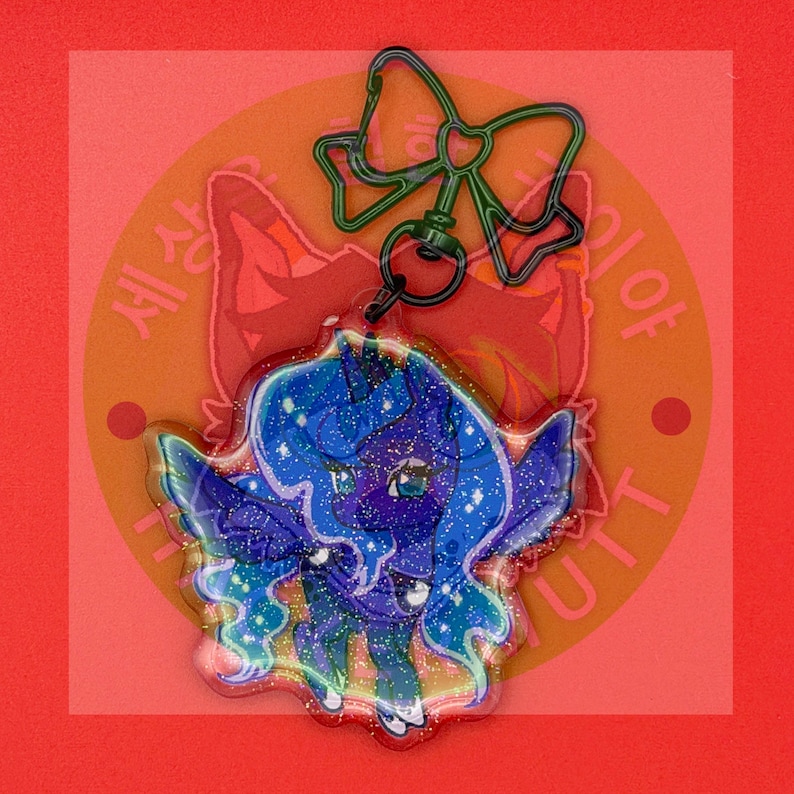 May include: A glittery acrylic keychain featuring a dark blue pony character with a flowing mane and wings, attached to a dark green metal bow-shaped clasp. The character has large eyes and a starry, cosmic pattern throughout its body and hair.
