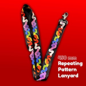 Puede incluir: Cordón negro con un patrón repetido de formas coloridas y estilizadas en forma de gusano. El cordón tiene un cierre de metal y el texto "450 mm Repeating Pattern Lanyard". El cordón mide aproximadamente 45 cm de largo.