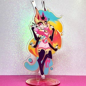 May include: A colourful acrylic stand featuring a cartoon character with pink, blue, and yellow hair, wearing a pink and white outfit, and standing on a colourful background.