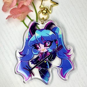 May include: A blue and purple anime character with black horns and a microphone, printed on a clear acrylic keychain.
