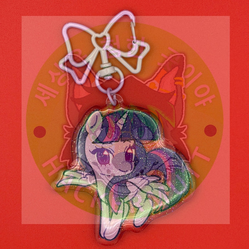 May include: A clear acrylic keychain featuring a glittery, cartoon-style unicorn character with a purple and blue mane. The charm is attached to a white, bow-shaped metal clasp. The character has large eyes and a stylized, colorful appearance.