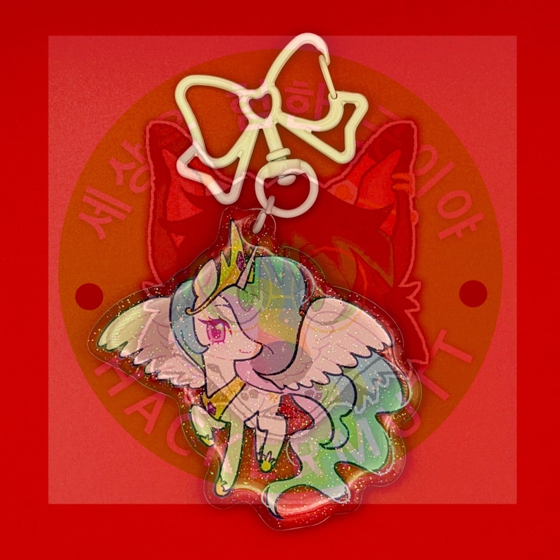 May include: An acrylic keychain featuring a cartoon alicorn with a golden crown, pink eyes, and a flowing multicolored mane. The character has large wings and is attached to a white plastic bow-shaped clasp. The surface has a glittery finish.