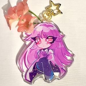 May include: A pink and purple anime-style character keychain with a star-shaped charm. The character has long purple hair, a white shirt, and black pants. The keychain is made of clear acrylic.