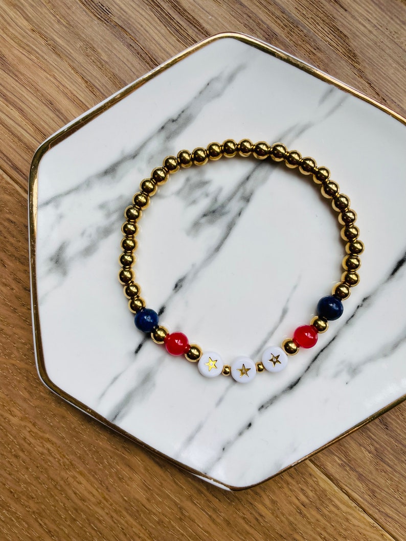 May include: Gold beaded bracelet with red, white and blue beads and gold stars on the white beads.
