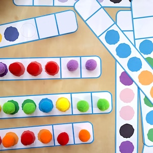 May include: A set of colourful pom-poms arranged in rows on a white background with blue borders. The pom-poms are in different colours, including red, orange, yellow, green, blue, and purple. The pom-poms are arranged in a pattern, with each row having a different number of pom-poms.